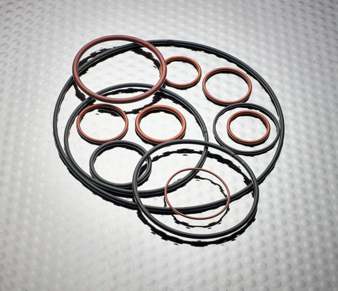 A group of red and black FEP Encapsulated O-Rings on a metal surface, with lighting focused on the middle and shadows visible.
