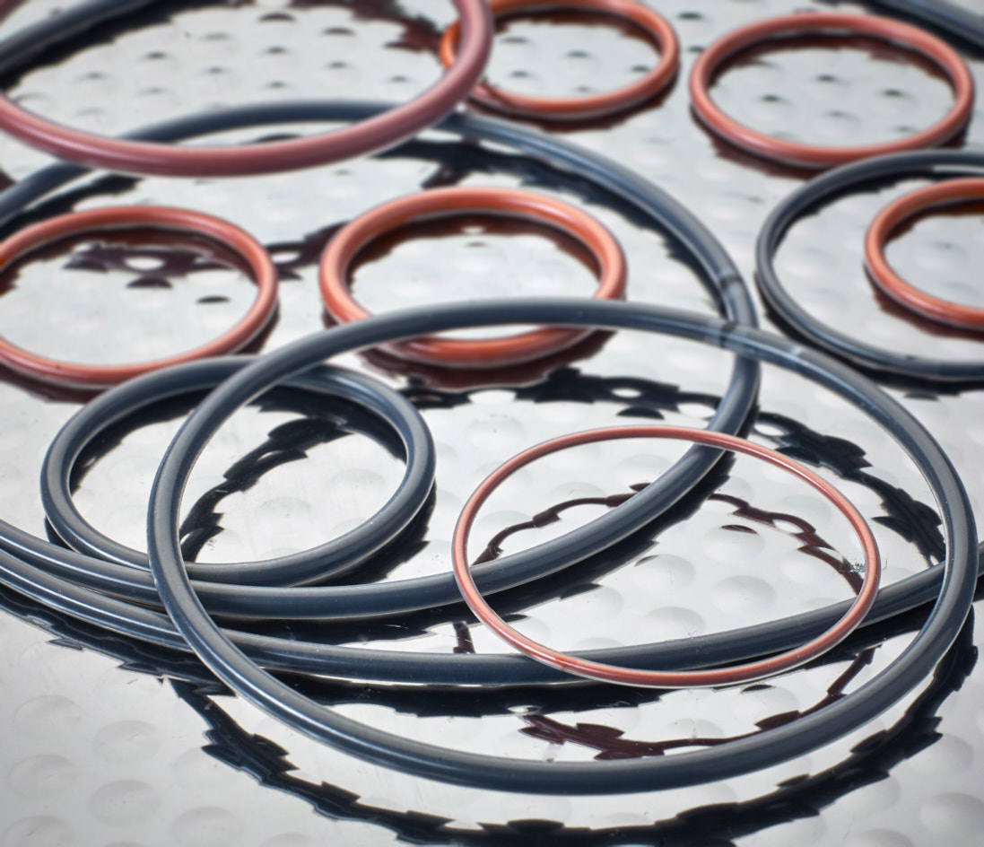 Several black or red FEP Encapsulated O-Rings arranged on a metal surface.